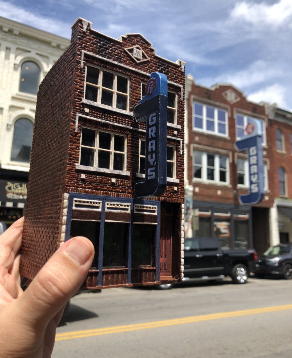 Hand-painted miniature of Gray's on Main held up in front of the real building
