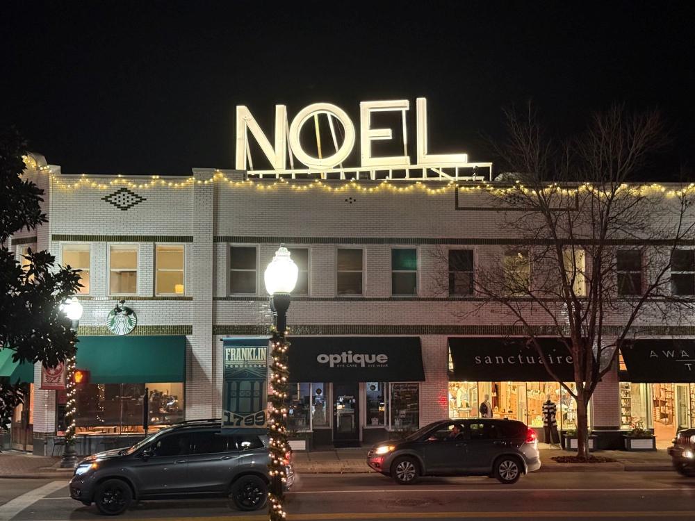The White Building at night during the holidays, with the lighted NOEL sign on the roof above the Starbucks and Main Street shops