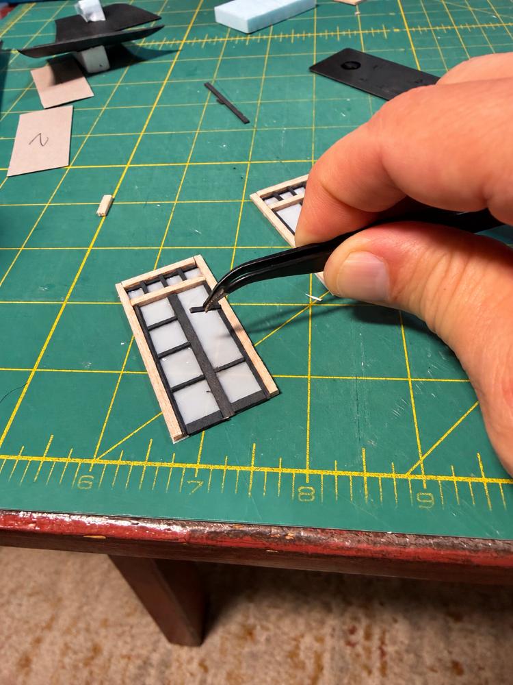 Hand-assembling tiny window frames for a Your Tiny Town miniature using tweezers at the workbench